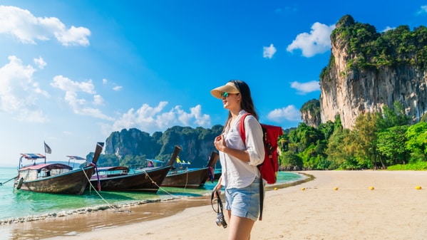 A young woman carrying a water bottle and wearing white glances out over the blue waters at phi phi island